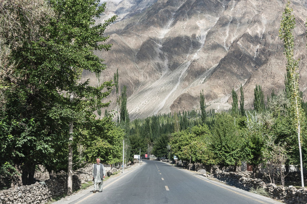 Weg door de Hunza-vallei in Baltistan, Pakistan, met groene bomen en hoge berghellingen op de achtergrond.