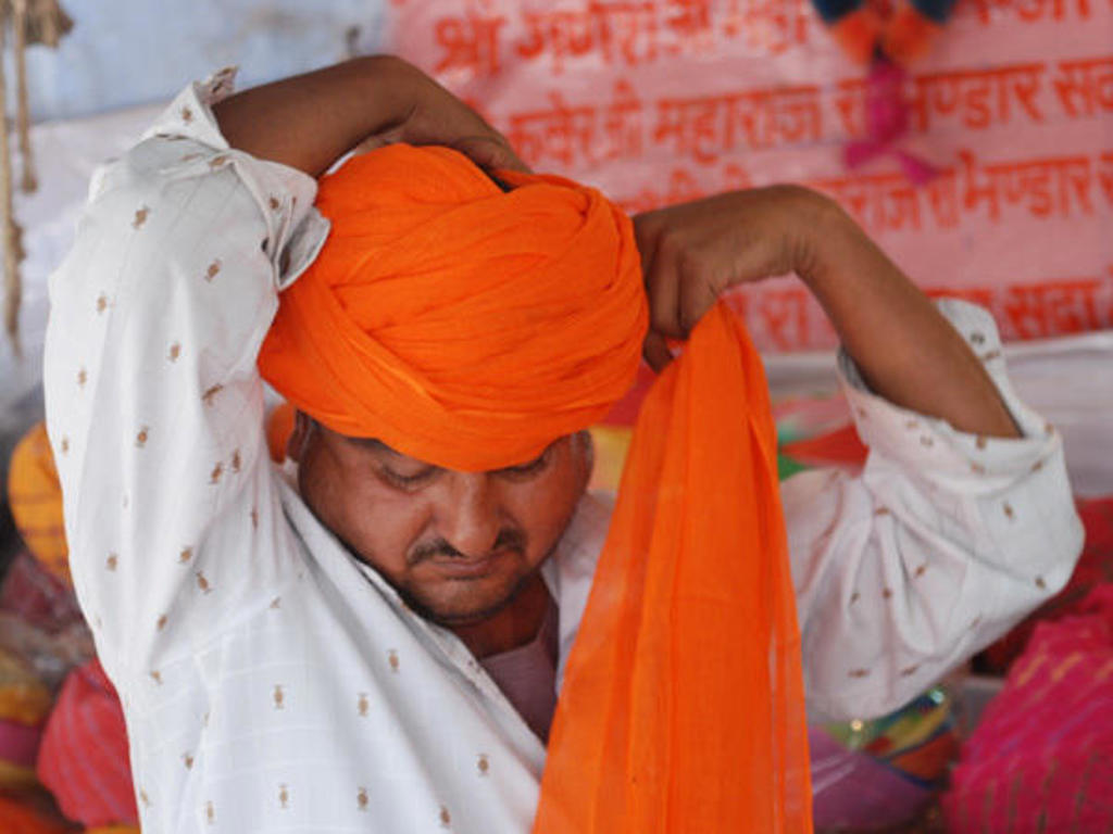 Man knoopt een oranje tulband op een kleurrijke markt tijdens een groepsrondreis langs hoogtepunten in Noord-India.