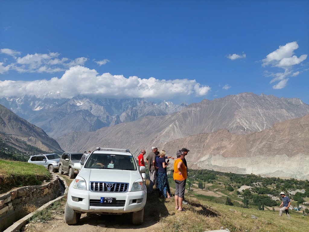 Groepsrondreis door de Hunza-vallei in Pakistan met jeeps en reizigers bij uitzicht op hoge bergen.