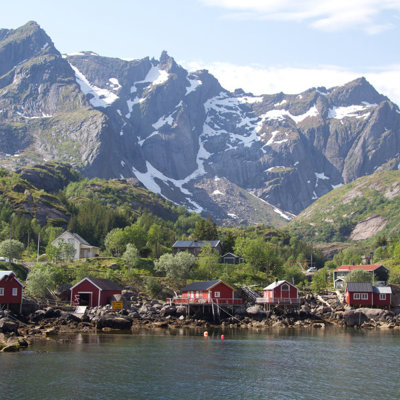 Rode vissershuisjes aan een fjord met groene bergen en besneeuwde toppen op de Faeröer eilanden.