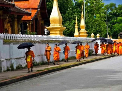 Boeddhistische monniken lopen langs een tempelmuur in Luang Prabang, Laos.