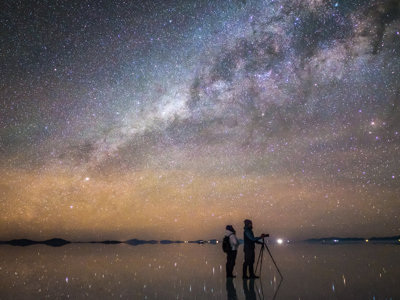 Sterrenhemel en Melkweg boven de Salar de Uyuni in Bolivia, met twee reizigers op het zoutmeer.
