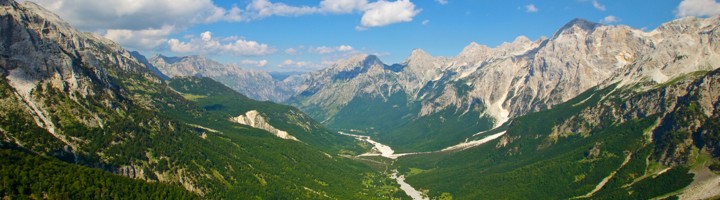 Panorama van de Valbona Valley in Albanië, met groene berghellingen, ruige toppen en een slingerende rivier.