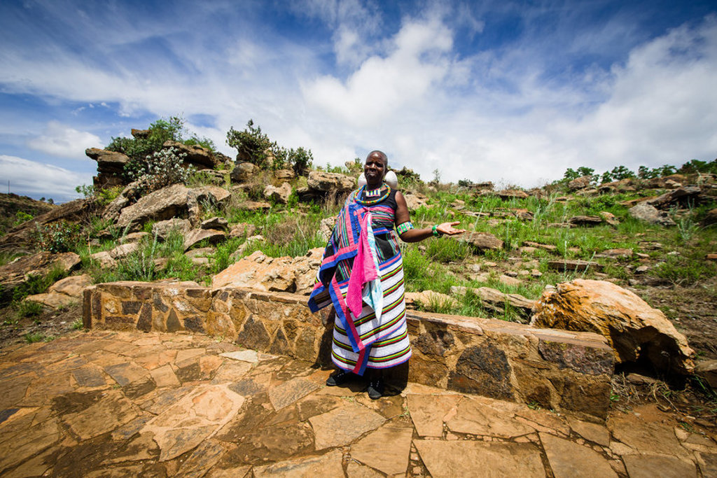 Traditioneel geklede vrouw in Lesotho bij rotsachtig landschap tijdens groepsrondreis Zuid-Afrika, eSwatini en Lesotho.