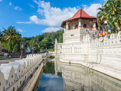 Tempel van de Tand in Kandy, Sri Lanka, met witte muren, vlaggen en reflectie in de gracht.