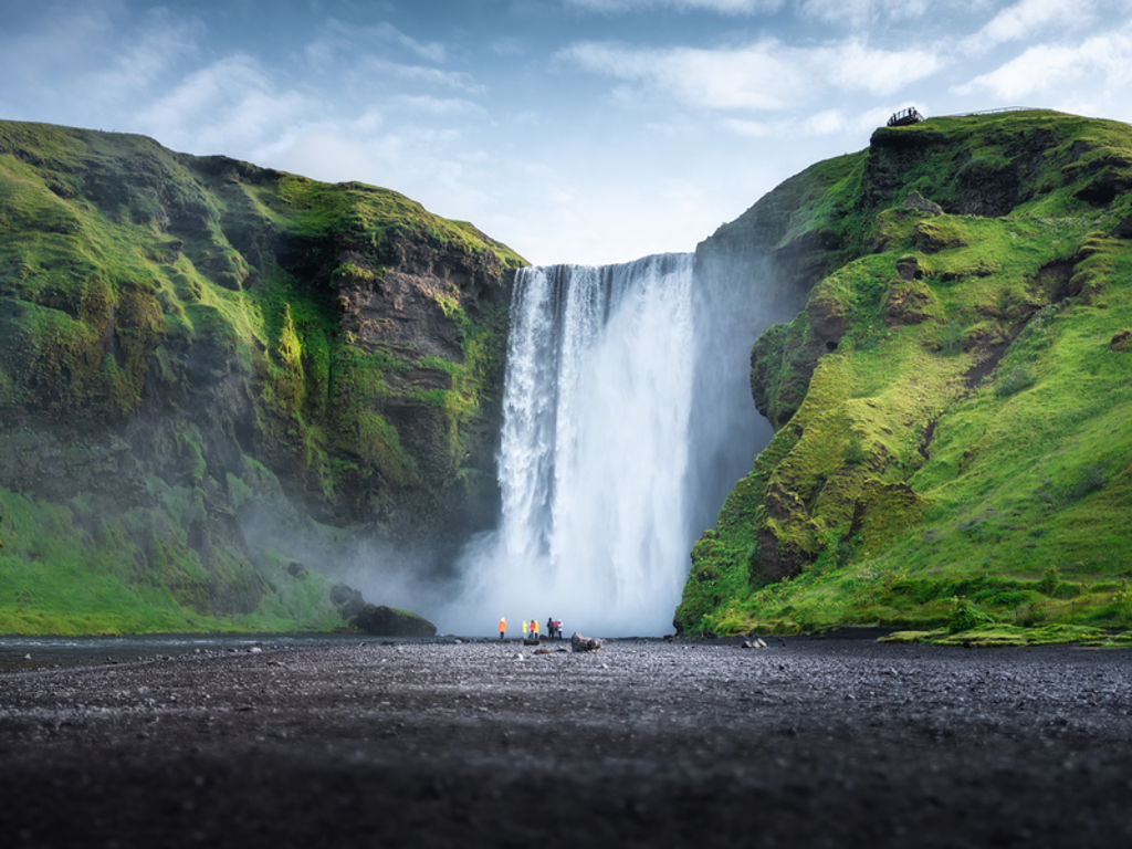 Skógafoss-waterval in IJsland met reizigers aan de voet, omringd door groene kliffen.