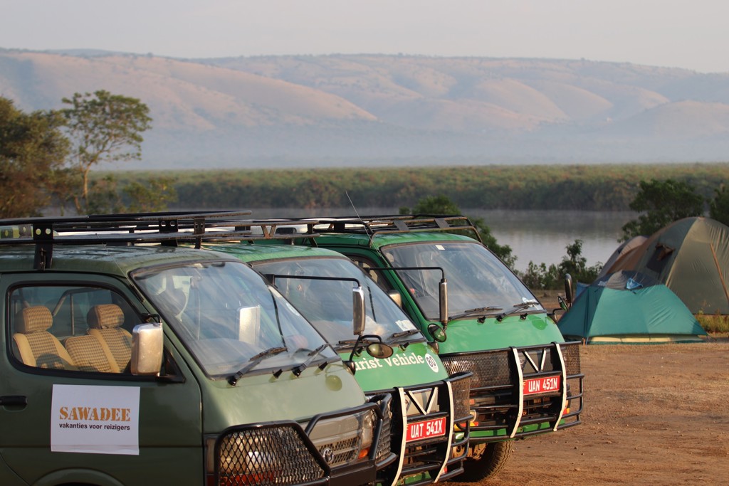 Safariwagens en tenten bij een kamp aan de rivier tijdens groepsrondreis Oeganda.