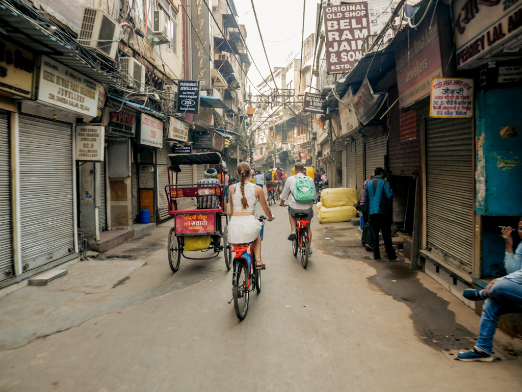 Jongvolwassenen fietsen door een smalle straat met riksja’s en winkels tijdens een 22-35ers reis in India.