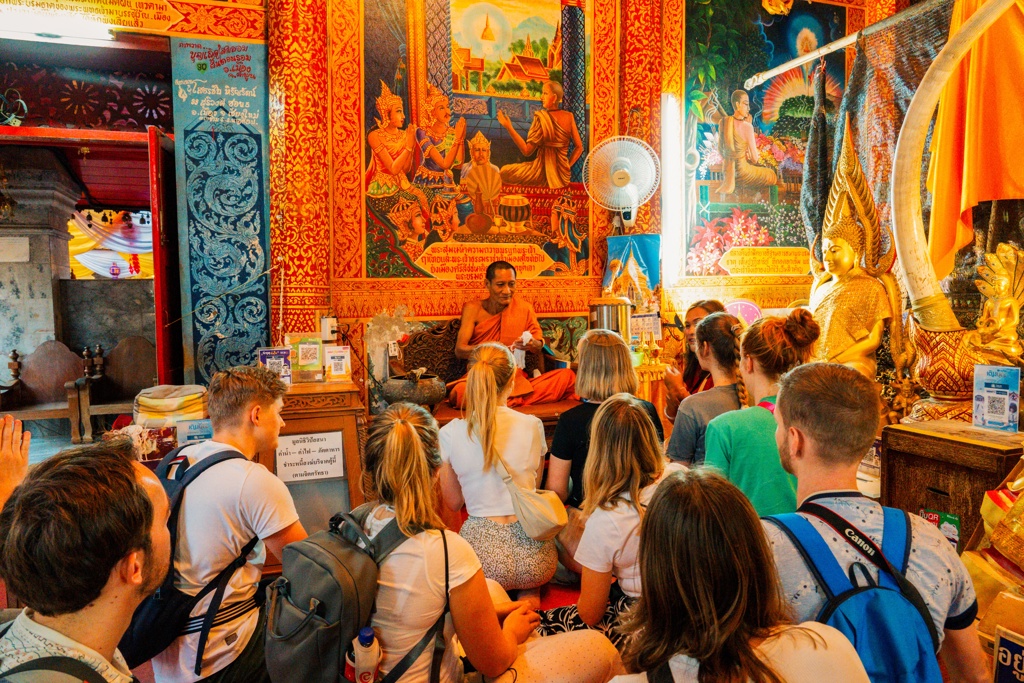 Jonge reizigers luisteren naar een boeddhistische monnik in een kleurrijke tempel tijdens een 22-35ers reis Thailand.