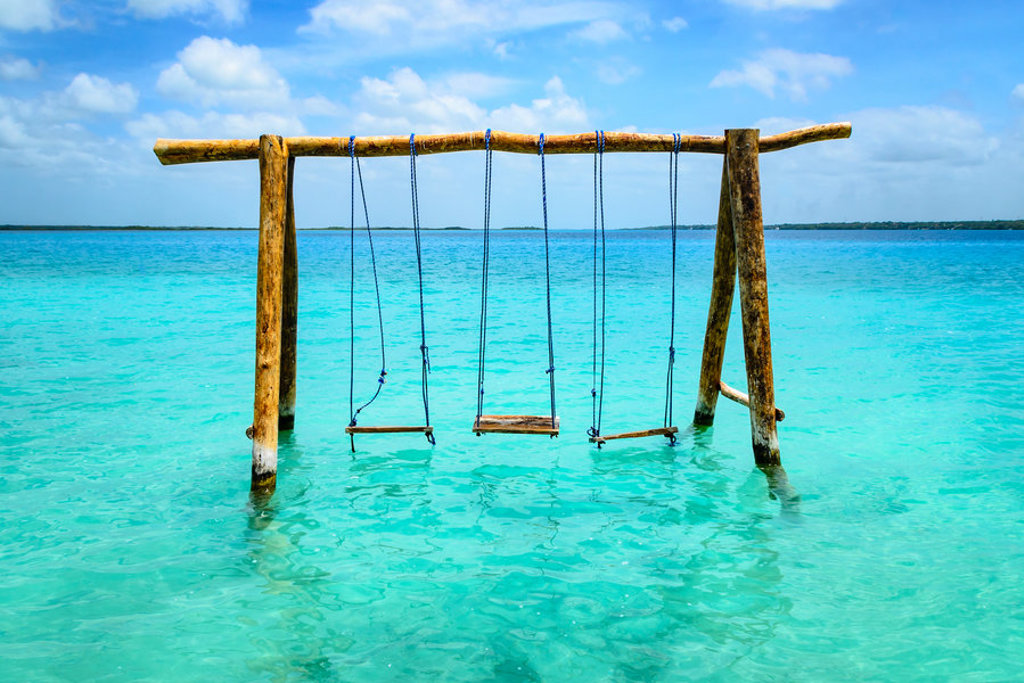 Houten schommel in turquoise zee bij Mexico, ideaal voor een familiereis langs de kust.