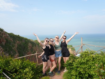 Vriendengroep poseert bij een uitzichtpunt met kliffen en zee in Thailand.