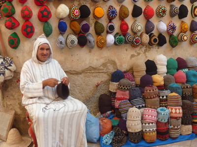 Marktverkoper in Marokko met kleurrijke gebreide mutsen aan de muur en opgestapeld op een kleed.