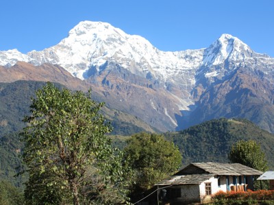Sneeuwtoppen van de Annapurna in Nepal met een huisje en groene heuvels op de voorgrond.