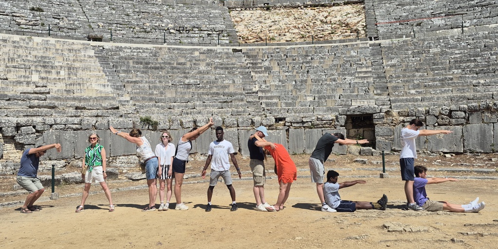 Groep reizigers poseert speels in het antieke theater van Epidaurus tijdens familiereis Noord-Griekenland.