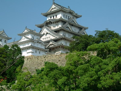 Wit Himeji-kasteel bovenop stenen muren, omringd door groene bomen in Japan.