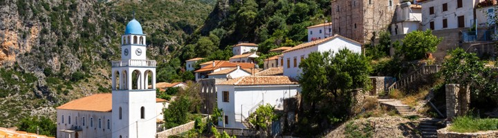 Kerk met blauwe koepel en witte huizen in het bergdorp Dhermi, Albanië.