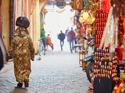 Vrouw loopt door smalle soukstraat met kleurrijke kraampjes in Marokko tijdens de Route Marokko Familiereis.