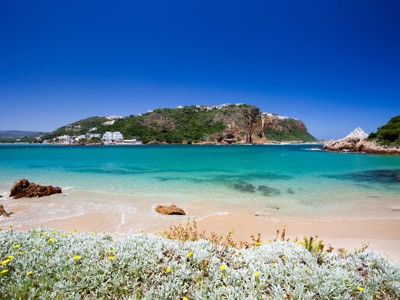 Uitzicht op Knysna Lagoon aan de Tuinroute in Zuid-Afrika, met turquoise water, strand en rotsen.