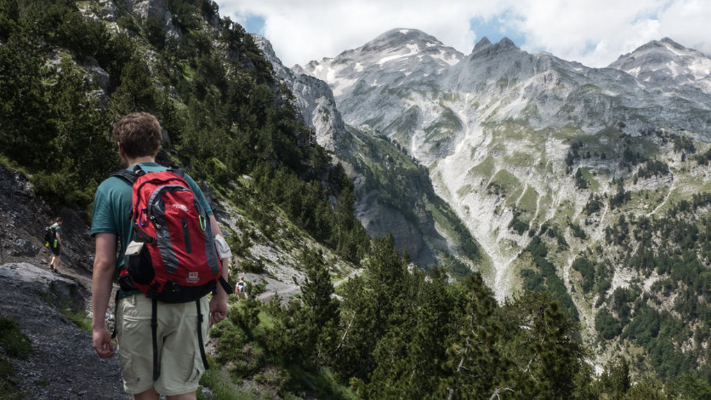 Wandelaar met rugzak op bergpad in de Peaks of the Balkan, met ruige bergtoppen op de achtergrond.