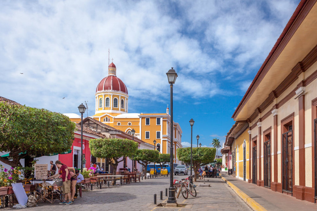 Straatbeeld in Granada, Nicaragua, met kleurrijke gebouwen en de kathedraal met rode koepel.