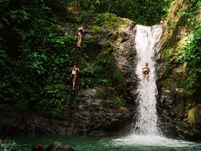 Avontuurlijke stop bij waterval in Costa Rica: reizigers klimmen en glijden in een natuurlijke pool.