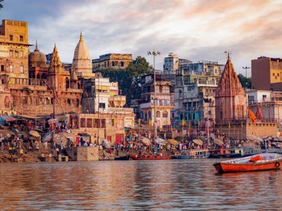 Ghats en tempels aan de Ganges in Varanasi bij zonsondergang, met boten op de rivier.