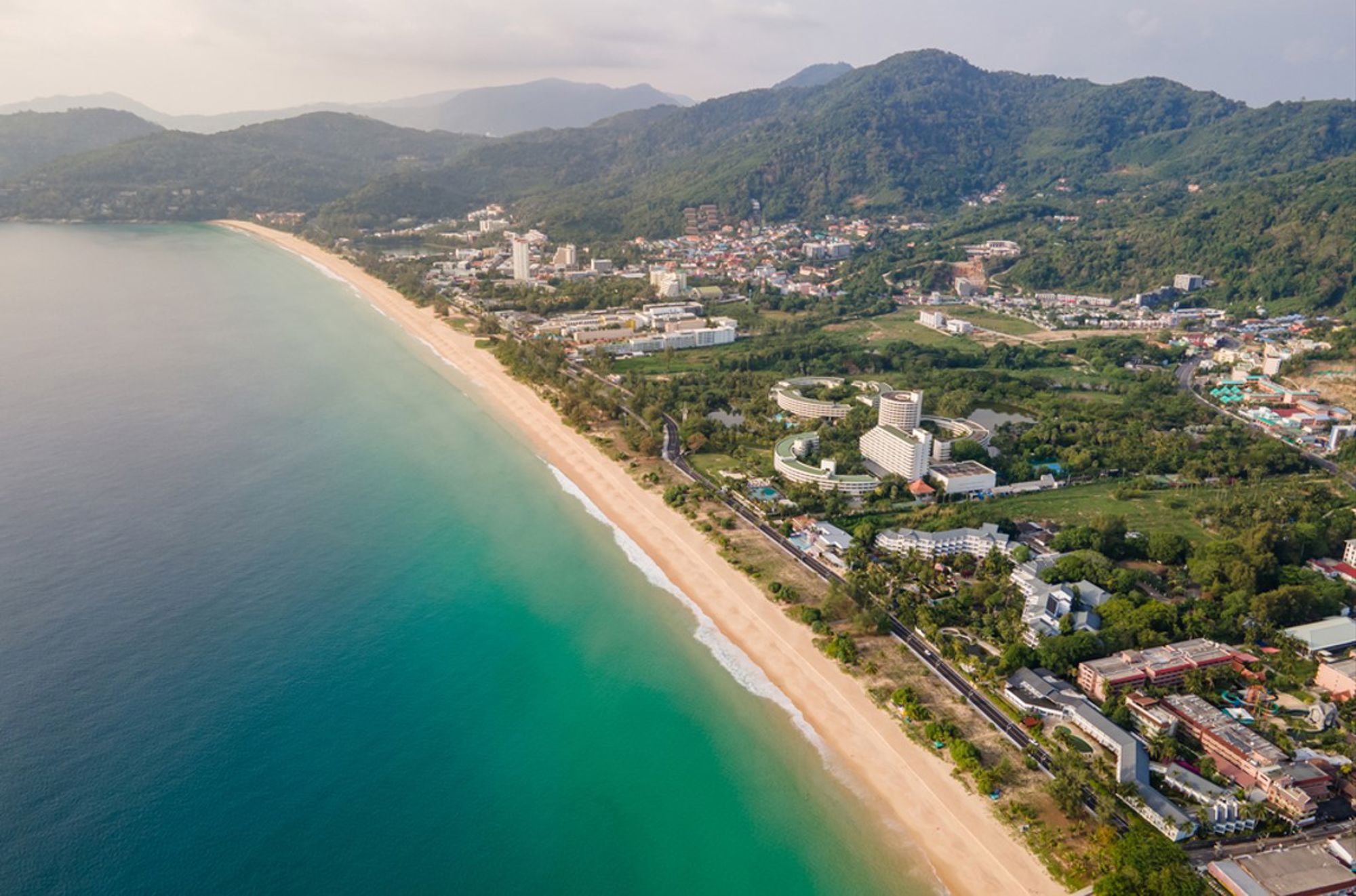 Patong Beach op Phuket, met lang zandstrand, turquoise zee en groene heuvels in Thailand.