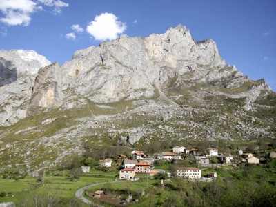 Berglandschap in de Picos de Europa met dorpje aan de voet van steile rotswanden onder blauwe lucht.