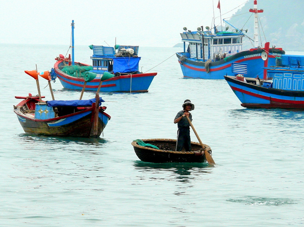 Vissersboten en een ronde boot op rustig water in Vietnam tijdens een fietsvakantie.