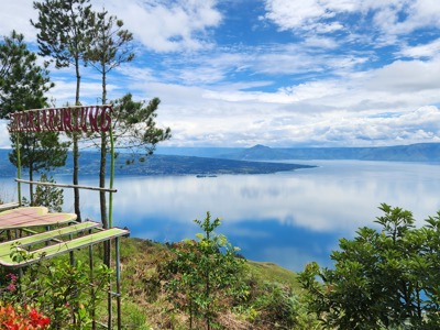 Uitzichtpunt over het Tobameer op Sumatra met helderblauw water, bergen en een wolkenlucht.