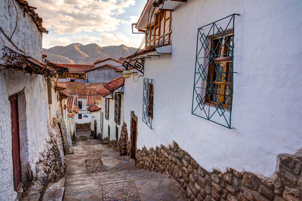 Straatje met witte huizen en rode daken in Cusco, Peru, met bergen op de achtergrond.