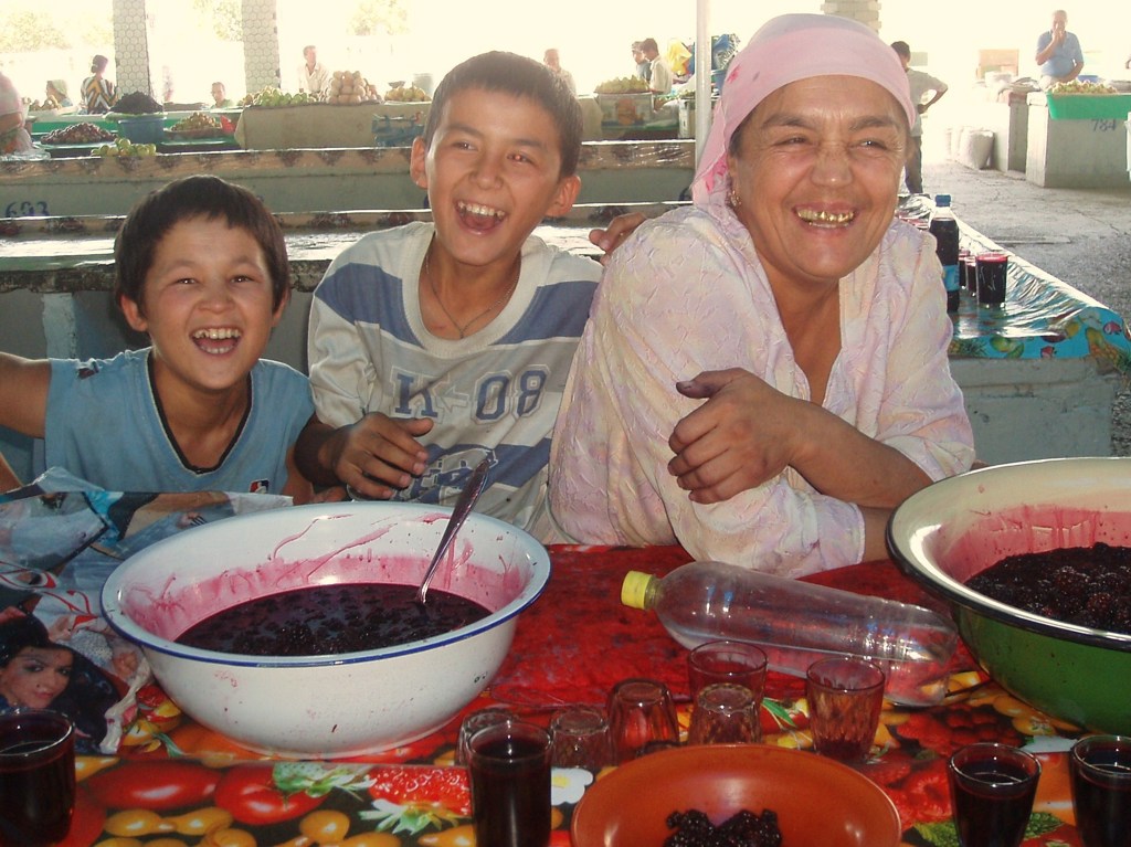Lachende familie aan tafel met fruit en drankjes op een lokale markt tijdens de groepsrondreis Zijderoute.