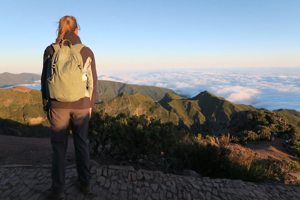 Wandelaar met rugzak kijkt uit over bergtoppen en wolkenzee op Madeira.