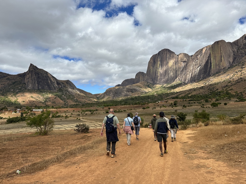 Wandelaars tijdens groepsrondreis Madagascar op zandpad met rijstvelden en rotsmassief van het Andringitra-gebergte.