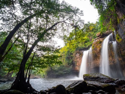 Waterval in groen regenwoud tijdens de route Thailand Avontuur 24 dagen, met rotsen en rivier op de voorgrond.