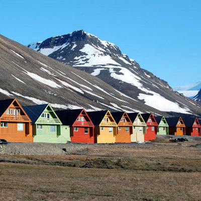 Gekleurde houten huisjes in Longyearbyen op Spitsbergen, met besneeuwde bergen op de achtergrond.