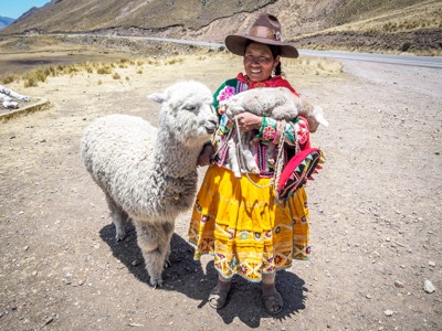Vrouw in traditionele kleding met alpaca en jong langs de route in de Peruaanse Andes tijdens Route Peru.