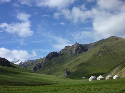 Groene bergvallei in Kirgistan met yurts onder een blauwe lucht.