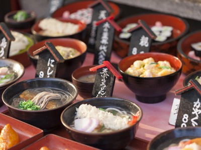 Japanse gerechten in kommetjes met prijskaartjes op een markt, zoals sobanoedels en sushi.