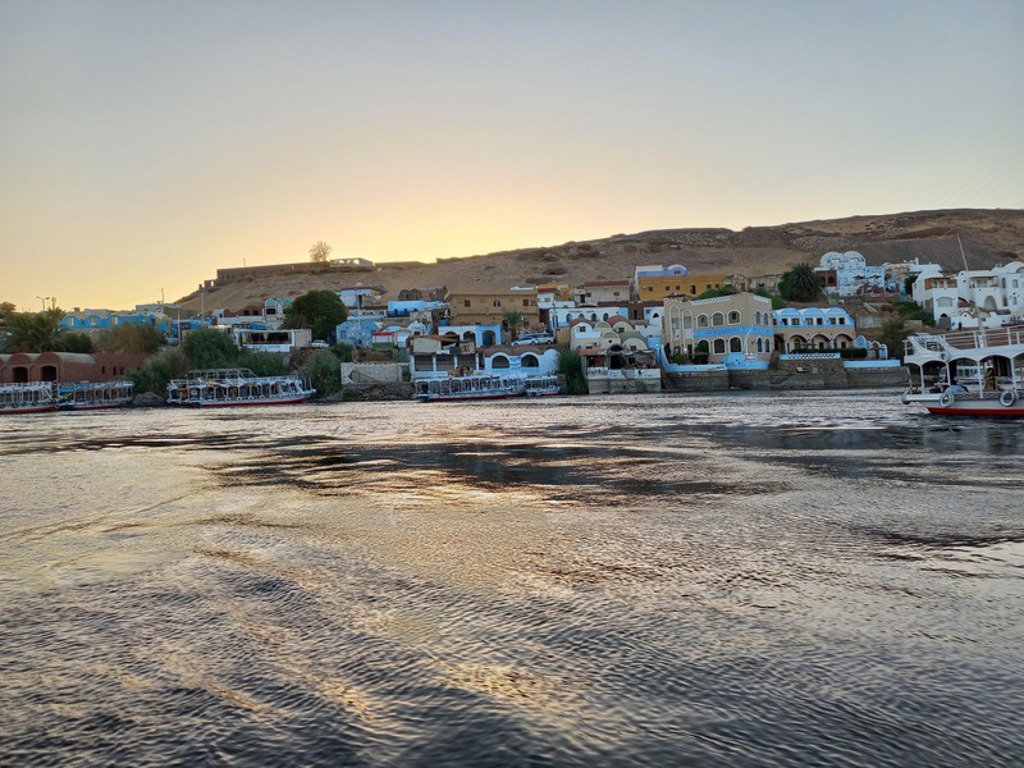 Zonsondergang over de Nijl met rivierboten en kleurrijke huizen langs de oever in Egypte.