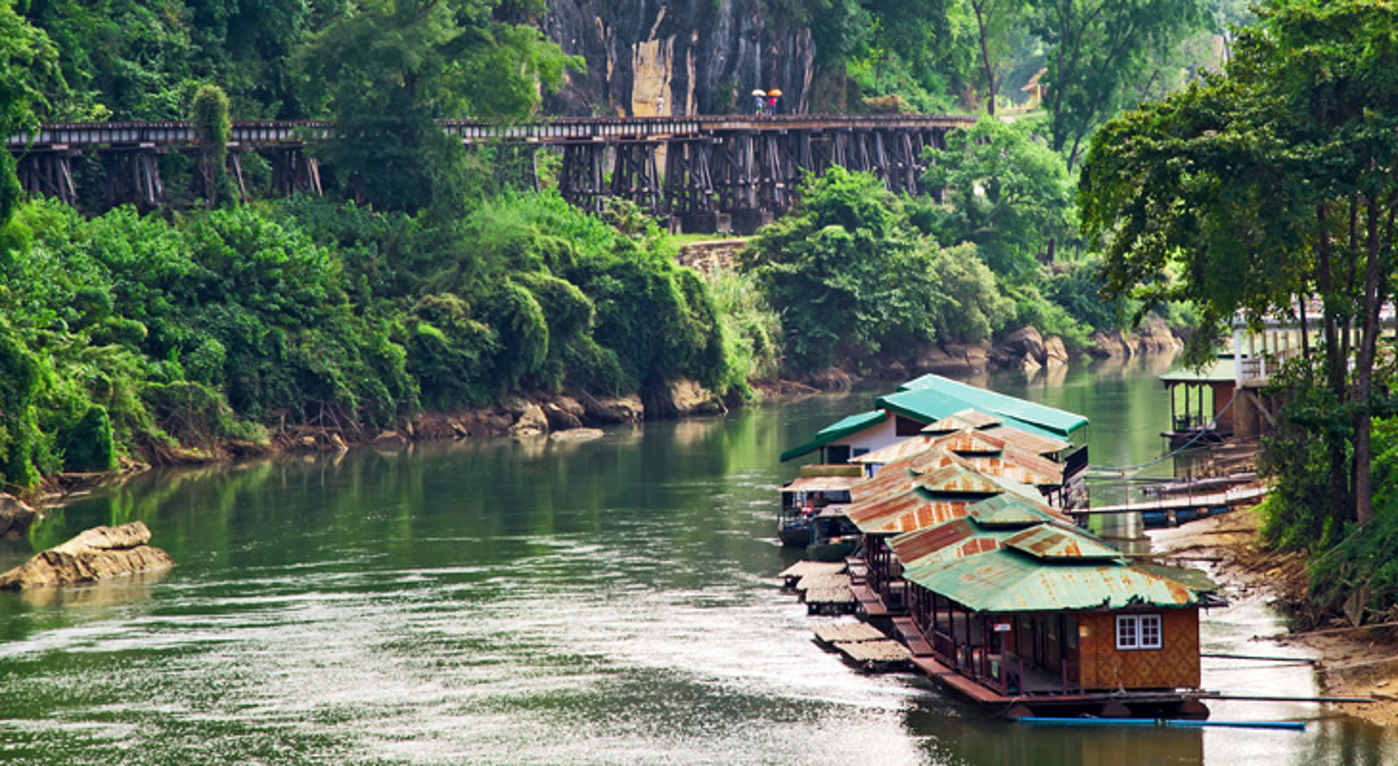 Drijvende huisjes op de River Kwai met de houten Death Railway-brug in Kanchanaburi, Thailand.