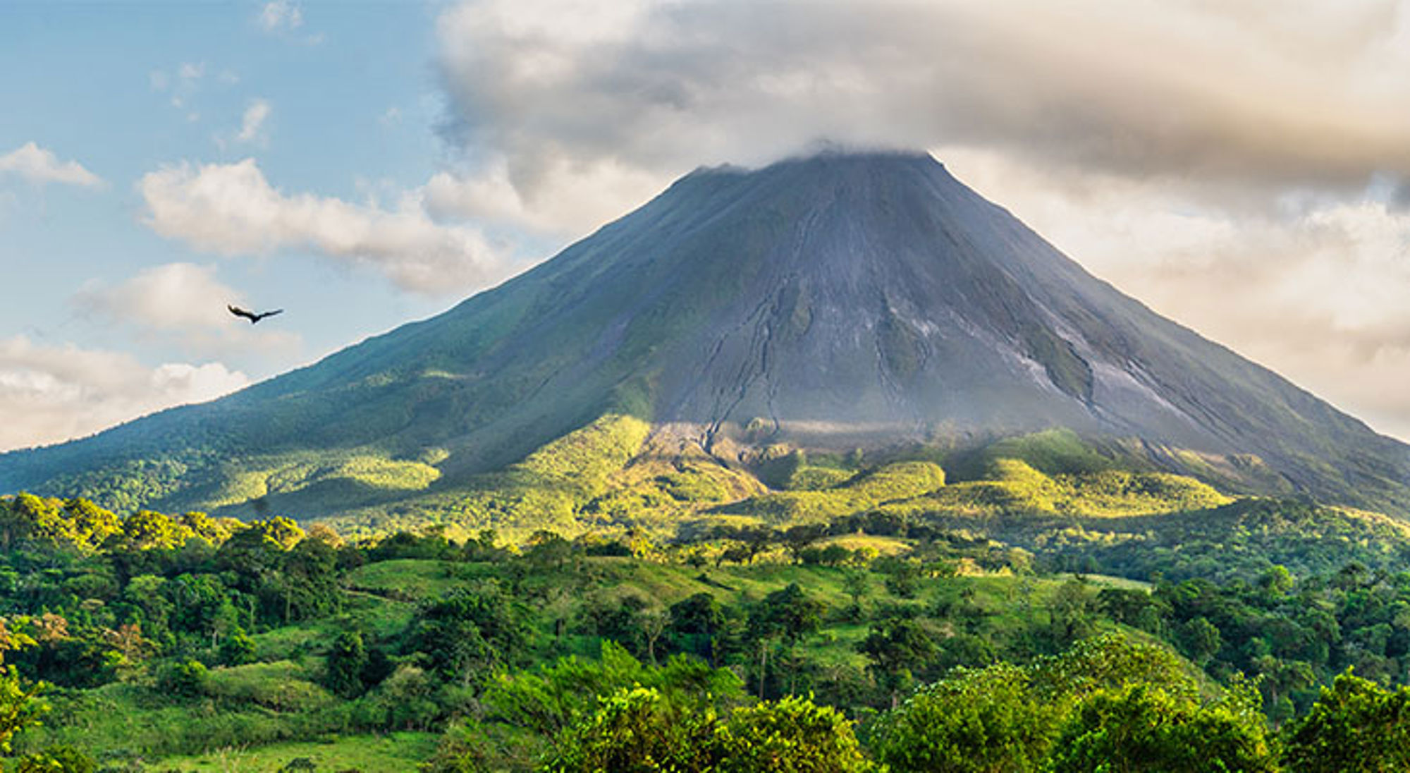 Arenal-vulkaan in Costa Rica boven groen regenwoud en heuvels onder een bewolkte lucht.