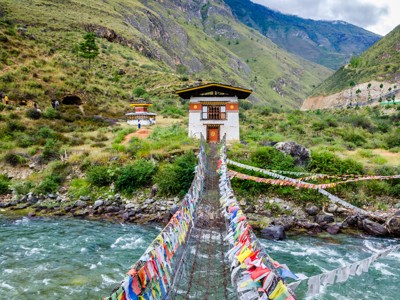 Hangbrug met gebedsvlaggen over een rivier in Bhutan, op de route Sikkim en Bhutan.