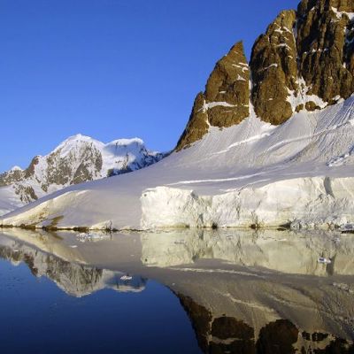 Besneeuwde bergtoppen en ijswand langs kalm water in Antarctica, tijdens een groepsrondreis per boot.