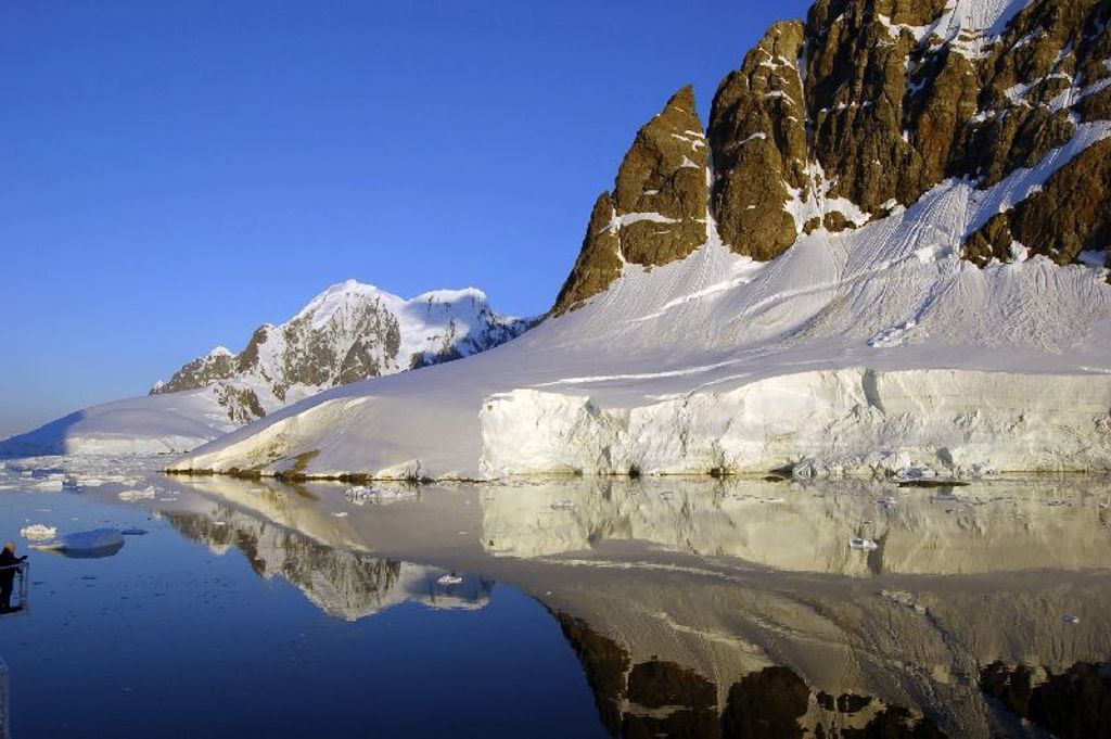 Besneeuwde bergtoppen en ijswand langs kalm water in Antarctica, tijdens een groepsrondreis per boot.