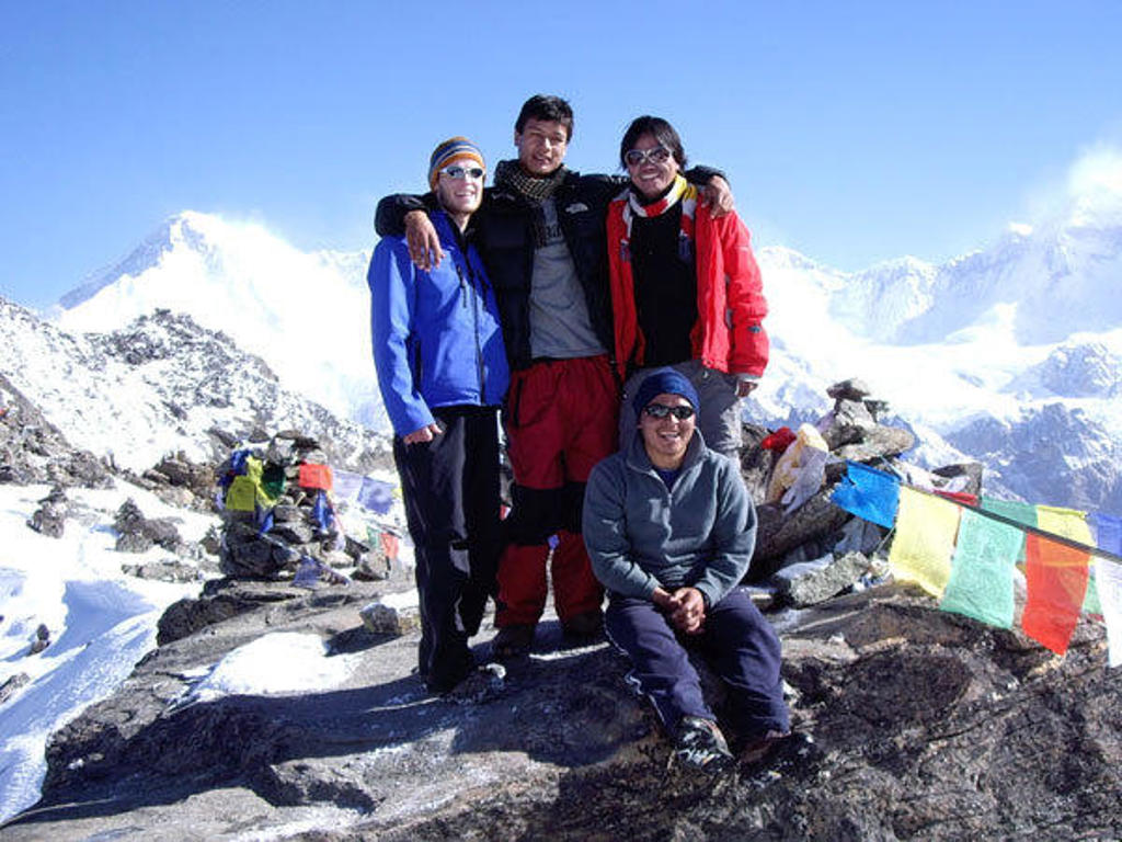 Groepsrondreis Nepal Everest: vier trekkers poseren op een besneeuwde bergkam met gebedsvlaggen.
