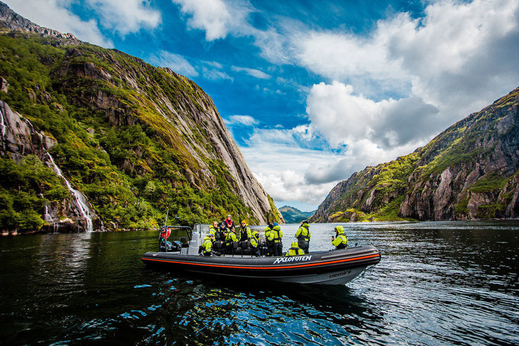 Groepsrondreis Noorwegen: boottocht door een fjord met steile bergwanden en waterval.