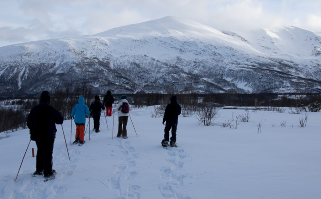 Groep wandelt met sneeuwschoenen door een besneeuwd Noors landschap met bergen op de achtergrond.