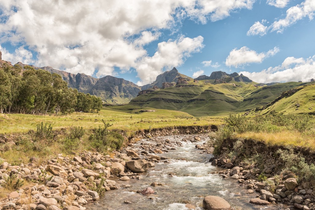 Berglandschap in Lesotho met een kabbelende rivier, groene heuvels en rotsformaties onder een blauwe lucht.