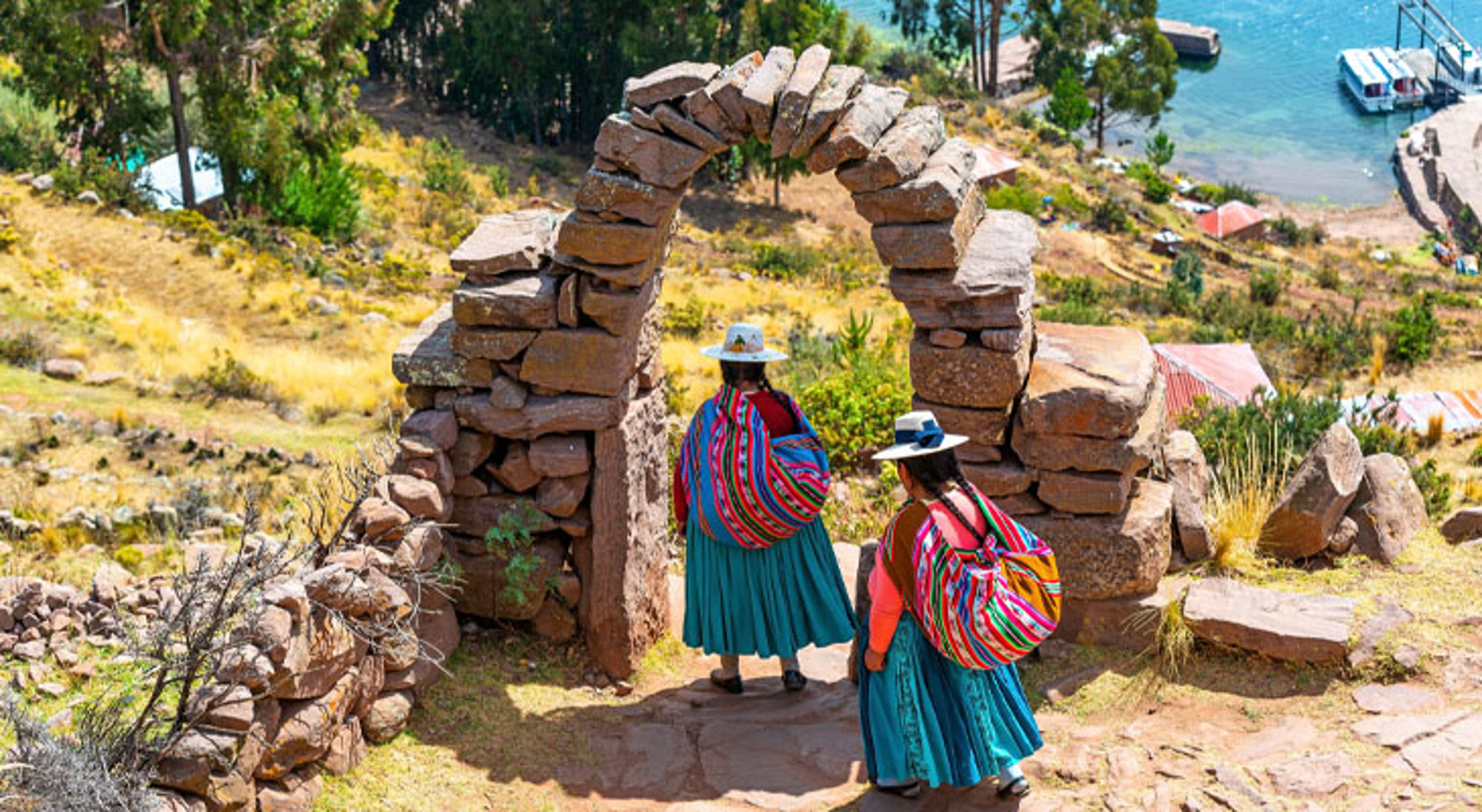 Quechua Titicacameer Twee vrouwen in traditionele kleding lopen door een stenen boog op het eiland Taquile bij het Titicacameer in Peru.